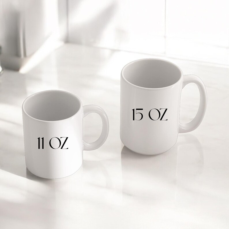 May include: Two white ceramic mugs with black text. The smaller mug is labeled "11 OZ" and the larger mug is labeled "15 OZ".