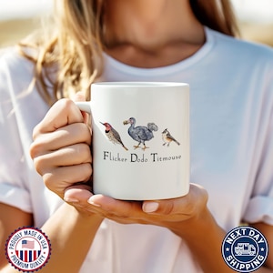 May include: White ceramic mug with a colorful illustration of a dodo, a flicker bird, and a titmouse. The text "Flicker Dodo Titmouse" is printed below the birds.