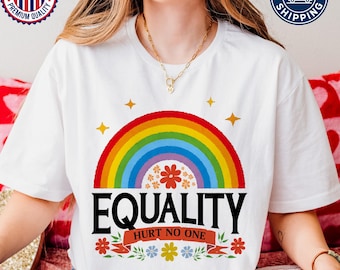 May include: White t-shirt featuring a vibrant rainbow design above the word "EQUALITY" in bold black letters. Below the text is "HURT NO ONE" on a banner with floral accents. The shirt has a crew neck.
