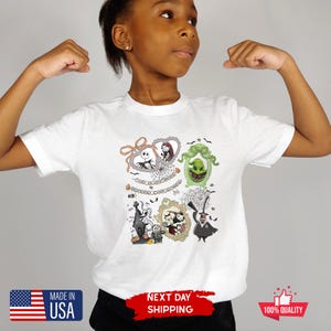 Może przedstawiać: Biała koszulka z kolorową grafiką postaci z filmu Miasteczko Halloween w ozdobnych ramkach. Koszulka zawiera tekst "MADE IN USA" i "NEXT DAY SHIPPING".