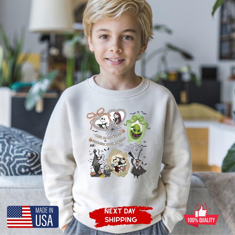 Może przedstawiać: Kremowa bluza z postaciami z kresk&oacute;wek w ramkach z filmu o tematyce Halloween. Projekt zawiera Jacka Skellingtona, Sally i inne postacie. Bluza ma napis "MADE IN USA" i "NEXT DAY SHIPPING".