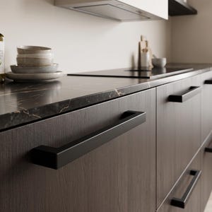 May include: A set of dark wood kitchen cabinets featuring long, horizontal matte black rectangular handles. The cabinets are topped with a black marble countertop with gold veining, holding a stack of ceramic bowls and a bottle of olive oil.