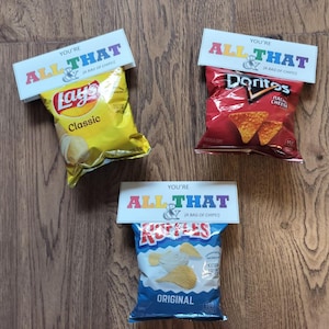 May include: Three bags of chips with attached cards that read "You're All That & (A Bag of Chips!)". The bags are Lay's Classic, Doritos Nacho Cheese, and Ruffles Original. The chips are on a wooden surface.