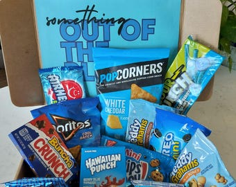 May include: A blue and white gift box filled with various snack foods, including animal crackers, white cheddar popcorn, Oreo cookies, and Hawaiian Punch flavored candy. The box is labeled "something out of the blue".