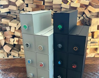 May include: Two vertical storage organizers with multiple drawers, one in light gray and one in black. Each drawer features a circular knob with a distinct colored icon representing different elements, including a tree, skull, sun, flame, and water drop.
