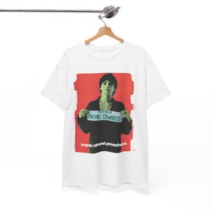 May include: White t-shirt with a graphic of Richie Edwards holding a sign with the text "4221401 RICHIE EDWARDS" against a red background. The words "manic street preachers" are printed below the image.