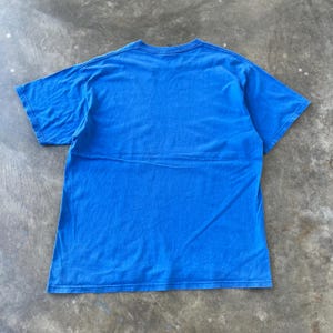 Pode incluir: Uma t-shirt de manga curta de cor azul brilhante s&oacute;lida com gola redonda. A pe&ccedil;a &eacute; exibida estendida, revelando a parte de tr&aacute;s da t-shirt, que apresenta uma superf&iacute;cie de tecido lisa sem padr&otilde;es com costuras padr&atilde;o nas mangas e na bainha.