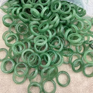 Könnte beinhalten: Eine große Ansammlung glatter, kreisförmiger Ringe aus durchscheinendem hellgrünem Stein. Die Ringe liegen verstreut in einem Haufen, wobei einige teilweise in einem durchsichtigen Plastikbeutel liegen. Jeder Ring hat eine polierte Oberfläche.