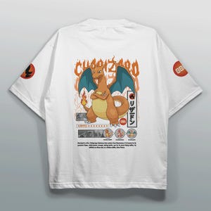 May include: White t-shirt featuring a Charizard graphic with orange and blue accents. The design includes Japanese text and a flame. The sleeves have circular designs with a red and black emblem.
