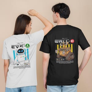 Può includere: Due persone indossano magliette con i disegni di WALL-E ed EVE di Disney Pixar. La maglietta bianca presenta EVE con testo, mentre la maglietta nera mostra WALL-E. Entrambe le magliette hanno la frase "DESIGNED TO LOVE".