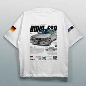 May include: White t-shirt featuring a silver BMW E30 car graphic with the text "MY DREAM CAR" and "BMW E30 1982-1994". The shirt also includes the German flag and BMW logo on the sleeves.