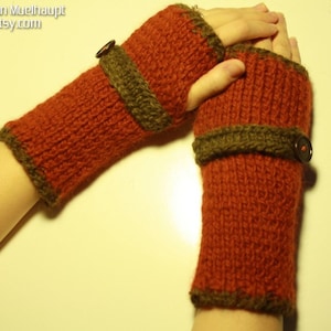 May include: A pair of knitted fingerless gloves with brown trim and a button detail. The gloves are a warm orange color.