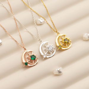 Pu&ograve; includere: Tre collane con ciondoli celesti in oro rosa, argento e oro. Ogni ciondolo presenta un design a mezzaluna e sole, con una gemma centrale. Le collane sono esposte su una superficie chiara.