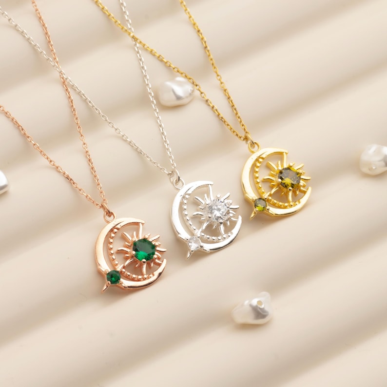 Pu&ograve; includere: Tre collane con ciondoli celesti in oro rosa, argento e oro. Ogni ciondolo presenta un design a mezzaluna e sole, con una gemma centrale. Le collane sono esposte su una superficie chiara.