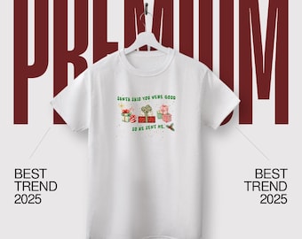 May include: White t-shirt featuring a festive graphic. The design includes the text "SANTA SAID YOU WERE GOOD SO HE SENT ME" above illustrations of wrapped gifts. The words "BEST TREND 2025" are on either side of the shirt.
