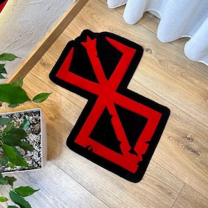 May include: A custom-shaped rug featuring the red Brand of Sacrifice symbol from the Berserk series set against a solid black background. The rug has a distinct angular design with sharp points and jagged edges, creating a bold graphic appearance.