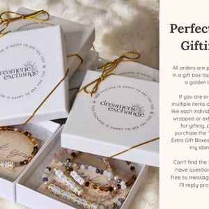May include: White gift boxes with gold ribbon and a logo that says "dreamerie exchange". The boxes contain beaded bracelets with letter beads that spell out "thank you". The text "Perfect for Gifting" is in the upper right corner of the image. The text below explains that all orders are packaged in a gift box topped with a golden bow.  The text also explains that extra gift boxes can be purchased for multiple items.
