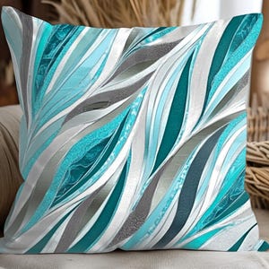 May include: Square cushion featuring a repeating pattern of teal, silver, and grey curved lines. The cushion has a soft, textured appearance, likely made of fabric. The design is abstract and modern, suitable for home decor.