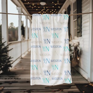 May include: A white blanket with the name "Weston" and the initials "WN" repeated in various shades of blue and gray. The blanket is hanging on a clothesline on a porch.