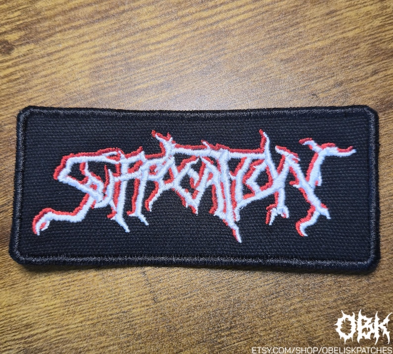 May include: Black rectangular patch embroidered with the word "SUFFOCATION" in white with a red outline. The patch has a black border and is likely for clothing or accessories. The Etsy shop name "OBK" is in the bottom right corner.