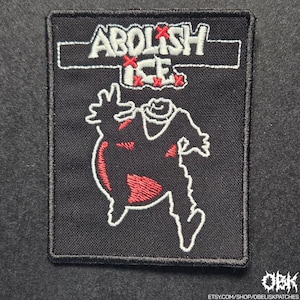 May include: Black rectangular patch with white embroidered text "ABOLISH ICE" above a red and white graphic of a figure. The figure has a red body and white outline. The patch is bordered in black.