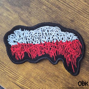 Può includere: Toppa ricamata con bordo nero, con un disegno nei colori della bandiera polacca: bianco e rosso. La sezione rossa presenta un design testuale stilizzato e gocciolante. La toppa ha il testo "OBK" e l'URL del negozio Etsy.
