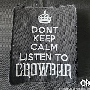 May include: Black square patch with white embroidered text and a crown graphic. The text reads "DONT KEEP CALM LISTEN TO CROWBAR". The patch is likely for a jacket or bag.
