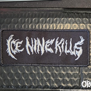 May include: A rectangular black patch with the text "Ice Nine Kills" embroidered in white, stylized with a gothic font. The patch is likely for clothing or accessories.