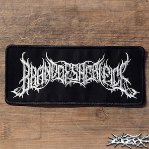 Puede incluir: Un parche rectangular negro bordado con texto blanco en una fuente de death metal estilizada, dentada y espinosa que dice Brand of Sacrifice. El parche tiene un borde grueso cosido en negro y una superficie de tela texturizada en todo el diseño.