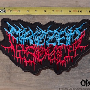 May include: A black embroidered patch featuring stylized text in light blue and red with a dripping, jagged aesthetic. A yellow measuring tape is positioned above the patch, showing it measures approximately 10.5 inches in total width.