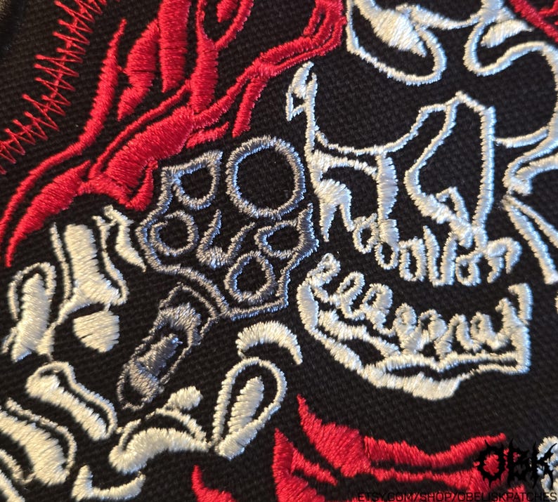 K&ouml;nnte beinhalten: Ein schwarzer Stoffaufn&auml;her mit detaillierter Stickerei eines wei&szlig;en Totenkopfes und einer Skeletthand, die einen Revolver h&auml;lt, akzentuiert durch leuchtend rote Flammenmuster. Unten rechts steht der Text "OBK" und "ETSY.COM/SHOP/OBELISKPATCHES".
