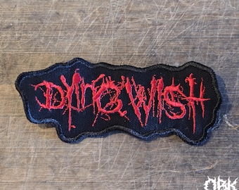 May include: A black embroidered patch with a jagged, irregular border. The text DYING WISH is stitched in a bright red, stylized, distressed font that resembles dripping paint or ink, featuring sharp, elongated lines and a textured appearance.