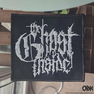 May include: Black square patch with white embroidered text that reads "the Ghost Inside". The patch has a gothic font style. The patch is likely for a jacket or bag.