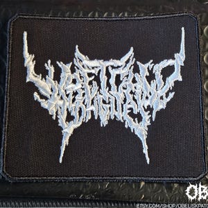 Pode incluir: Um emblema retangular bordado em preto com fio branco formando um design de texto estilizado, irregular e ilegível no centro. O emblema tem uma borda preta espessa costurada e cantos arredondados sobre uma base de tecido texturizado.