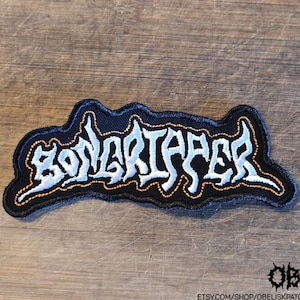 May include: An embroidered patch featuring the word BONGRIIPER in stylised white lettering with a thin orange border on a black background. The patch has a jagged, irregular shape and includes the text etsy.com/shop/obeliskpatches in the corner.