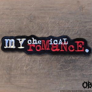 May include: An embroidered fabric patch featuring the text My Chemical Romance in a stylized font. The letters are stitched in a combination of white and red thread against a black background, with a small white dot at the end of the text.
