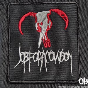May include: A square black embroidered patch featuring a silver and red stylized skull design at the top. Below the skull, the text Job For A Cowboy is stitched in a jagged, white, metallic-style font. The patch has a black stitched border.