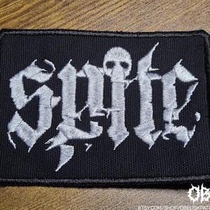 May include: Black rectangular patch with the word "Suffer" embroidered in white gothic lettering. A skull is incorporated into the design. The patch has a black border and is likely for clothing or accessories.