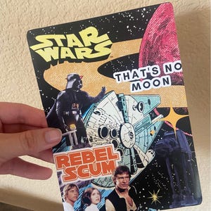 May include: A Star Wars sticker with images of Darth Vader, the Millennium Falcon, and other characters. The sticker includes the text "Star Wars", "That's No Moon", and "Rebel Scum". The background is a space scene.