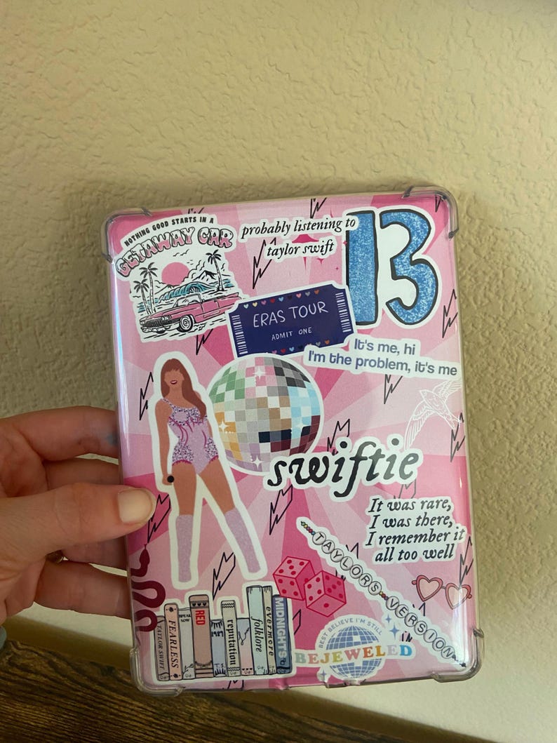 May include: A pink phone case with a variety of colorful stickers, including a pink car, a disco ball, a heart, and a ticket for the Eras Tour. The case also features the text "probably listening to taylor swift" and "swiftie".