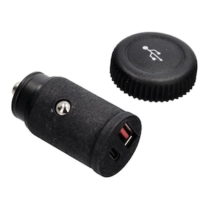 Może przedstawiać: Czarna ładowarka samochodowa z teksturowanym uchwytem i oddzielną nasadką. Ładowarka posiada port USB i mały srebrny przycisk. Nasadka posiada symbol USB.