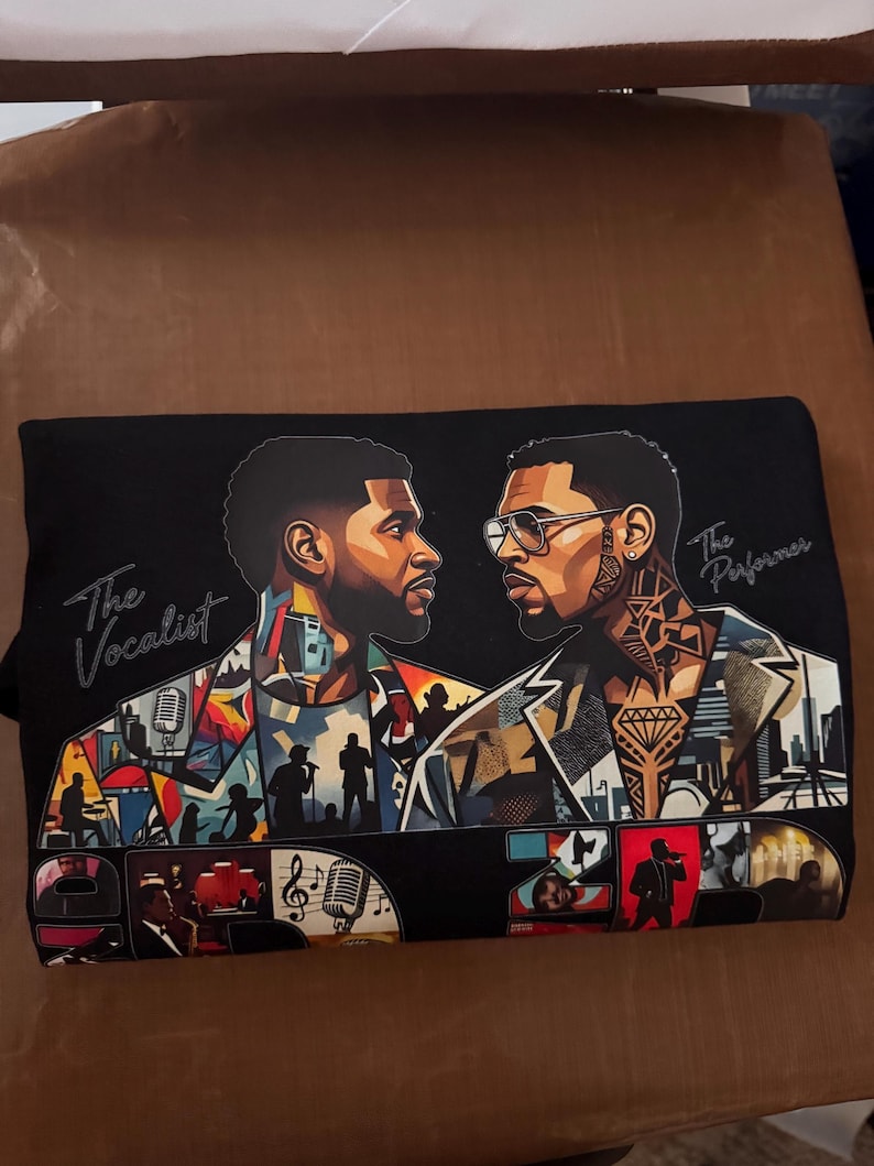 May include: A black t-shirt featuring a graphic illustration of two men facing each other. The left figure is labeled The Vocalist, and the right figure is labeled The Performer. The design includes colorful collage-style imagery of microphones, cityscapes, and musical silhouettes.