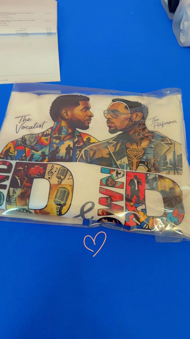 May include: A white t-shirt in a clear plastic bag featuring a graphic print of two men facing each other. The text reads The Vocalist and The Performer. The design includes colorful collage elements, musical instruments, microphones, and large letters.