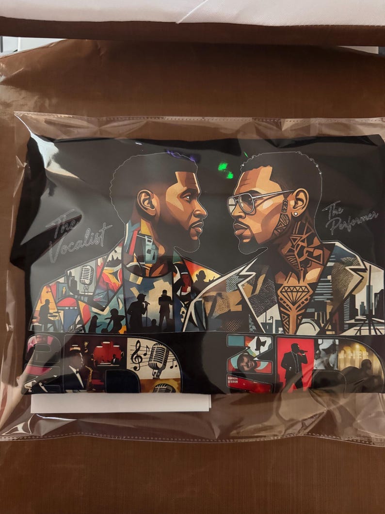 May include: A black t-shirt featuring a graphic illustration of two men facing each other. The left side shows a man labeled The Vocalist with a microphone, while the right side shows a man labeled The Performer wearing glasses. The design includes colorful collage elements of musical scenes and cityscapes.