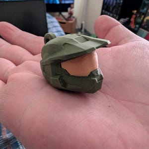 May include: A green plastic 3D printed replica of a Master Chief helmet from the Halo video game series.