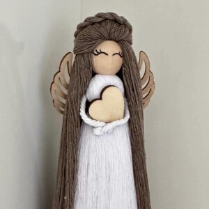May include: A brown yarn angel doll with white yarn dress and wooden wings holding a wooden heart.