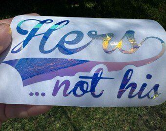 May include: A white vinyl sticker with iridescent rainbow lettering that reads "Hers... not his".