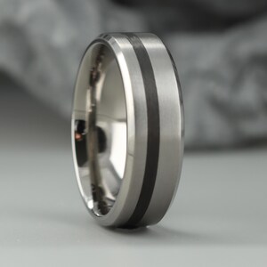 Ehering aus Titan und schwarzer Kohlefaser mit abgeschrägter Kante. Mitte mattiert, Ränder poliert. Wohlfühlpass innen. KOSTENLOSE GRAVUR.