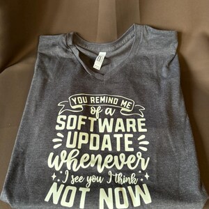May include: A dark gray V-neck t-shirt with a white graphic that reads "You remind me of a software update whenever I see you I think not now".