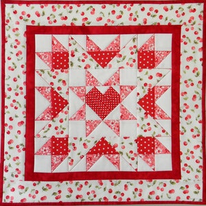 May include: A red and white patchwork quilt with a cherry print border. The quilt is made up of squares and triangles, and features a large heart in the center.